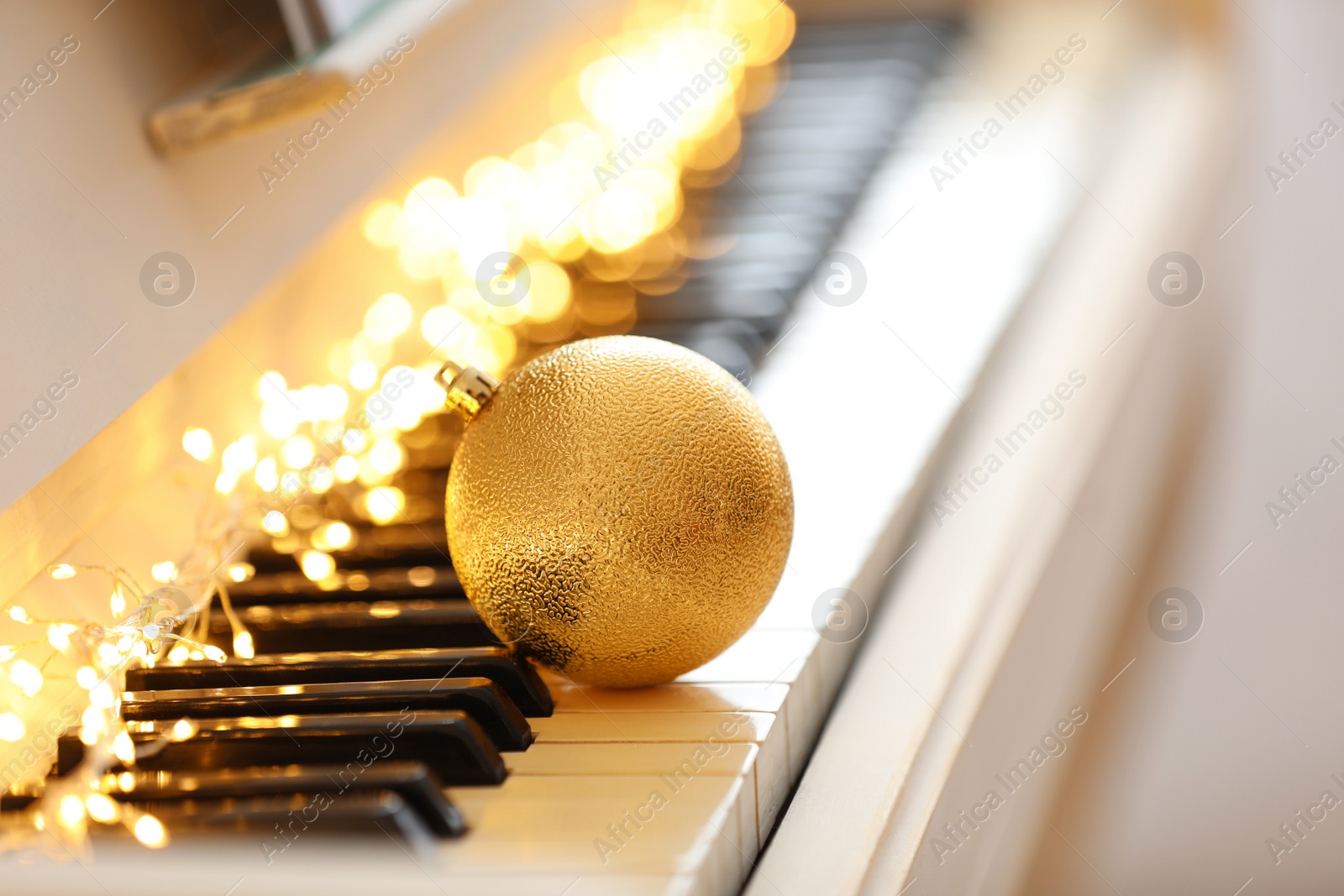 Photo of Beautiful golden bauble and fairy lights on piano keys, space for text. Christmas music