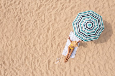 Image of Woman resting under striped beach umbrella at sandy coast, aerial view. Space for text