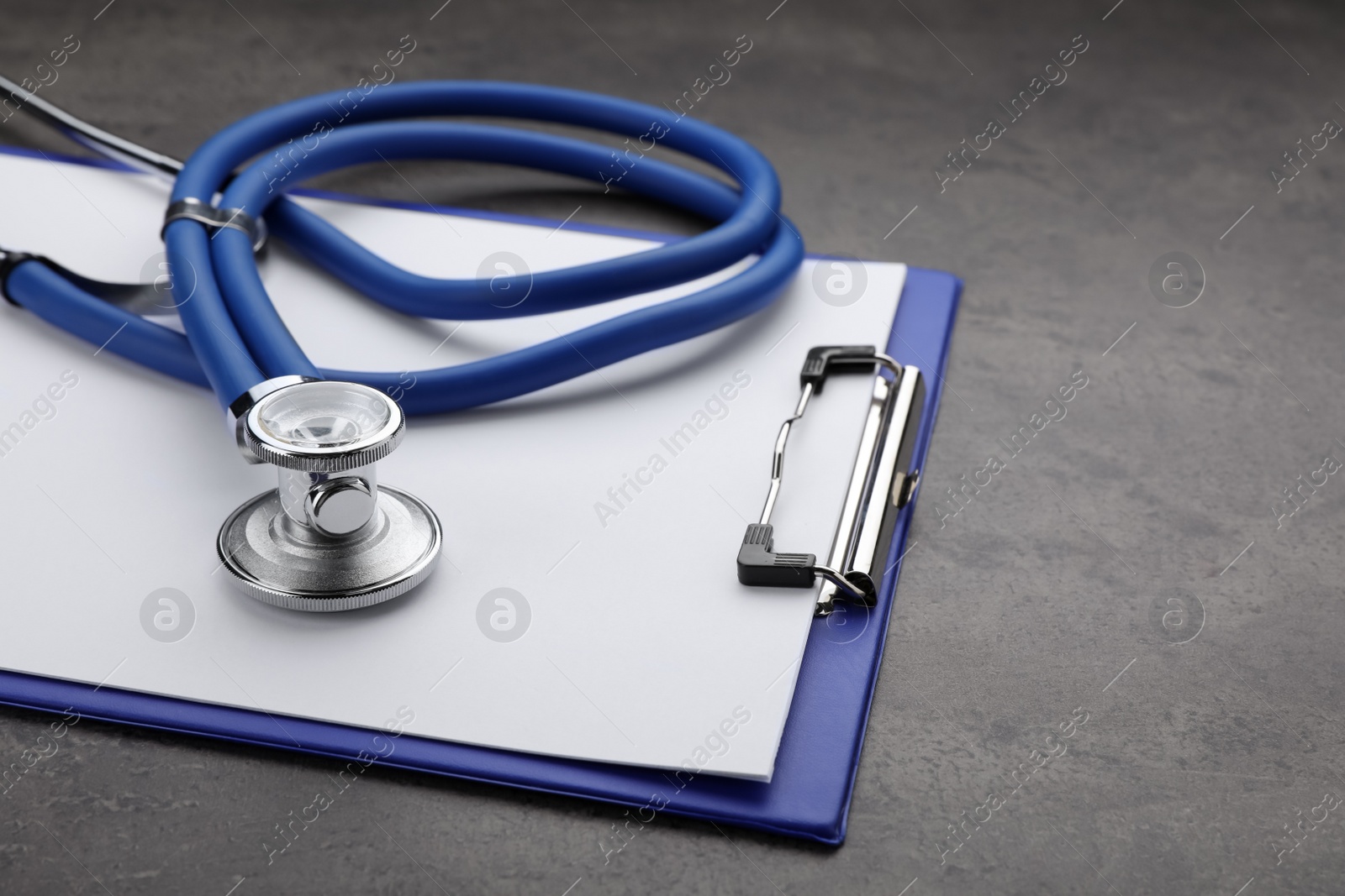 Photo of Clipboard with stethoscope on grey table, closeup