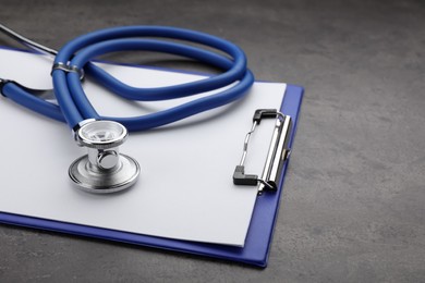 Photo of Clipboard with stethoscope on grey table, closeup