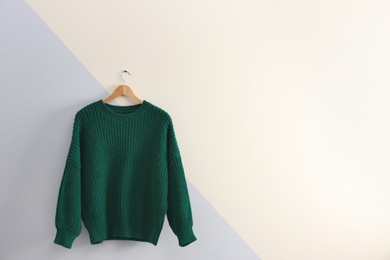 Photo of Hanger with stylish sweater on color wall. Space for text