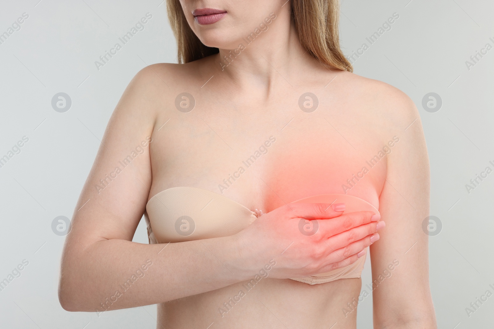 Image of Young woman suffering from breast pain on light grey background, closeup