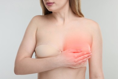 Young woman suffering from breast pain on light grey background, closeup