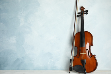 Photo of Beautiful violin and bow on white wooden table near light blue wall. Space for text