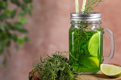 Photo of Mason jar of homemade refreshing tarragon drink with lemon slices and sprigs on wooden stump, closeup. Space for text