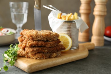 Photo of Tasty schnitzels served with knife and french fries on grey table, closeup. Space for text
