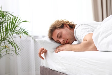 Handsome young man sleeping on pillow at home, space for text. Bedtime