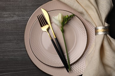 Stylish table setting. Plates, cutlery, napkin and floral decor on dark wooden background, top view