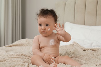 Photo of Cute little child with cream on skin in bedroom