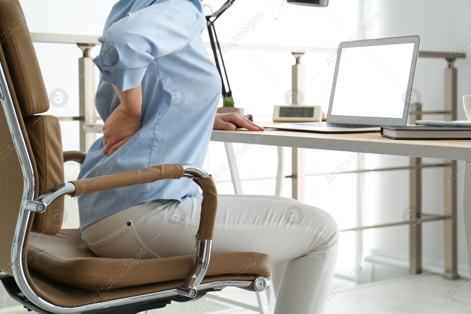 Photo of Woman suffering from back pain at workplace in office, closeup