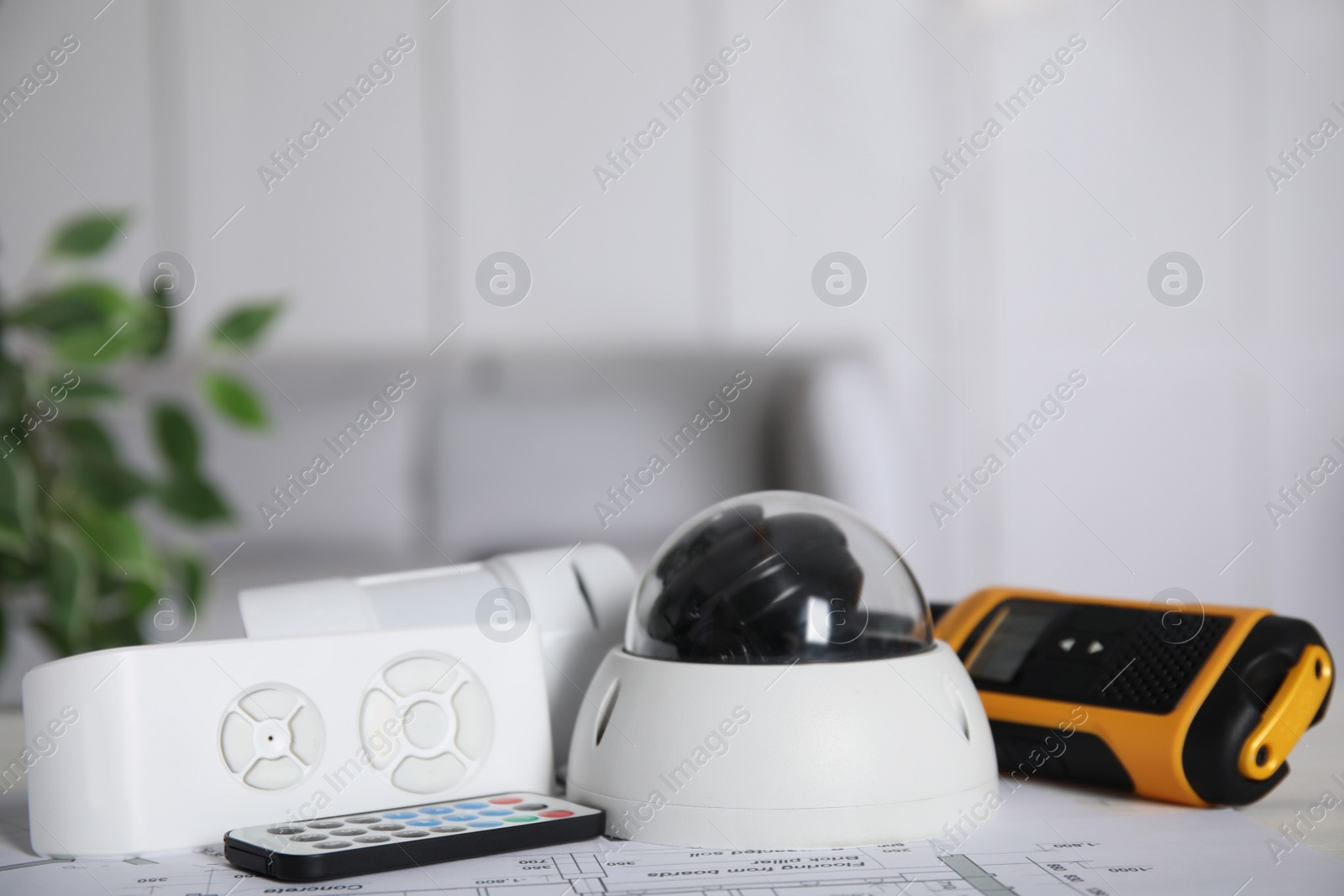 Photo of CCTV camera, remote controls, movement detector and walkie talkie on building plan indoors. Home security system