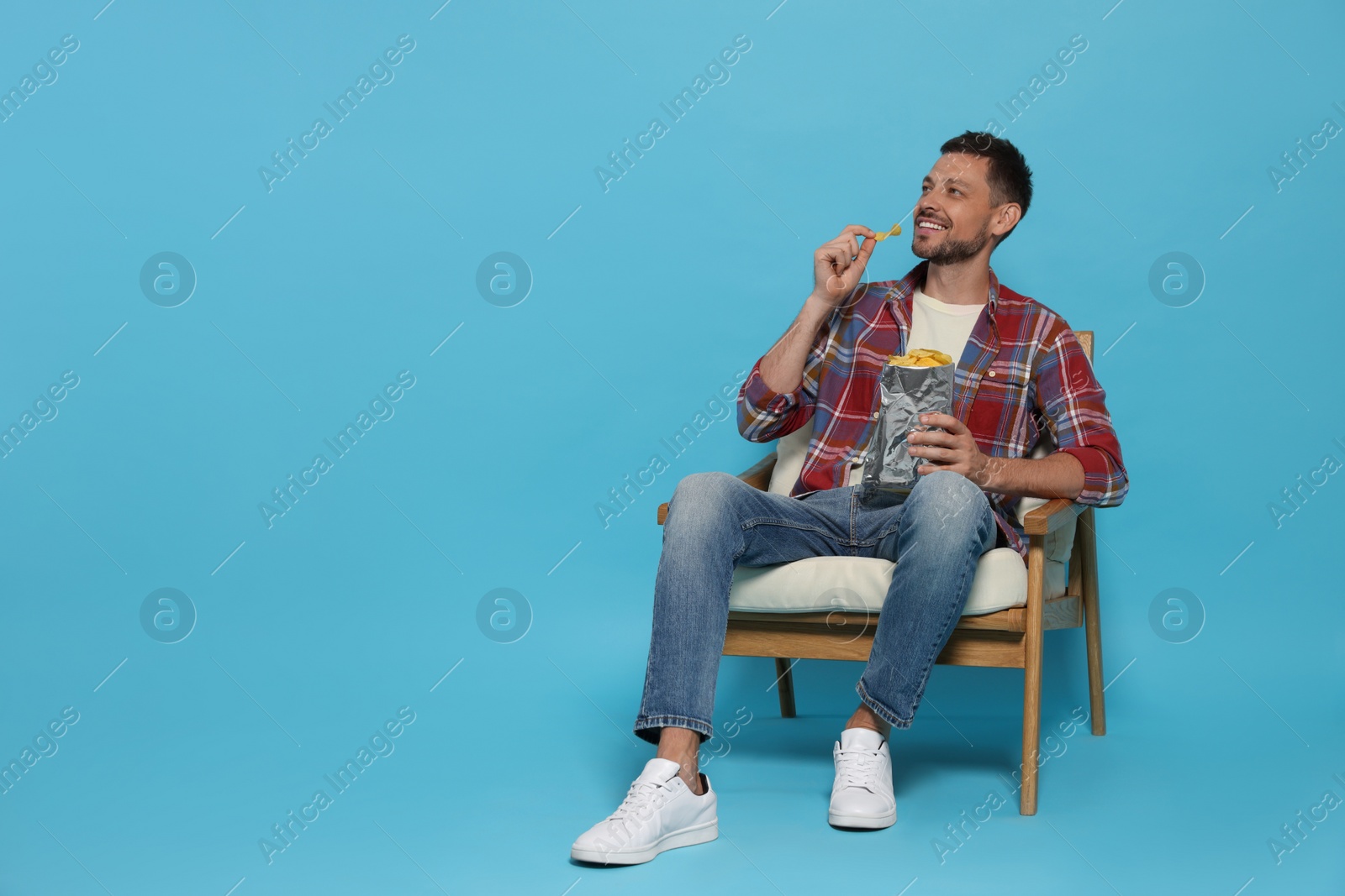 Photo of Handsome man eating potato chips on light blue background, space for text