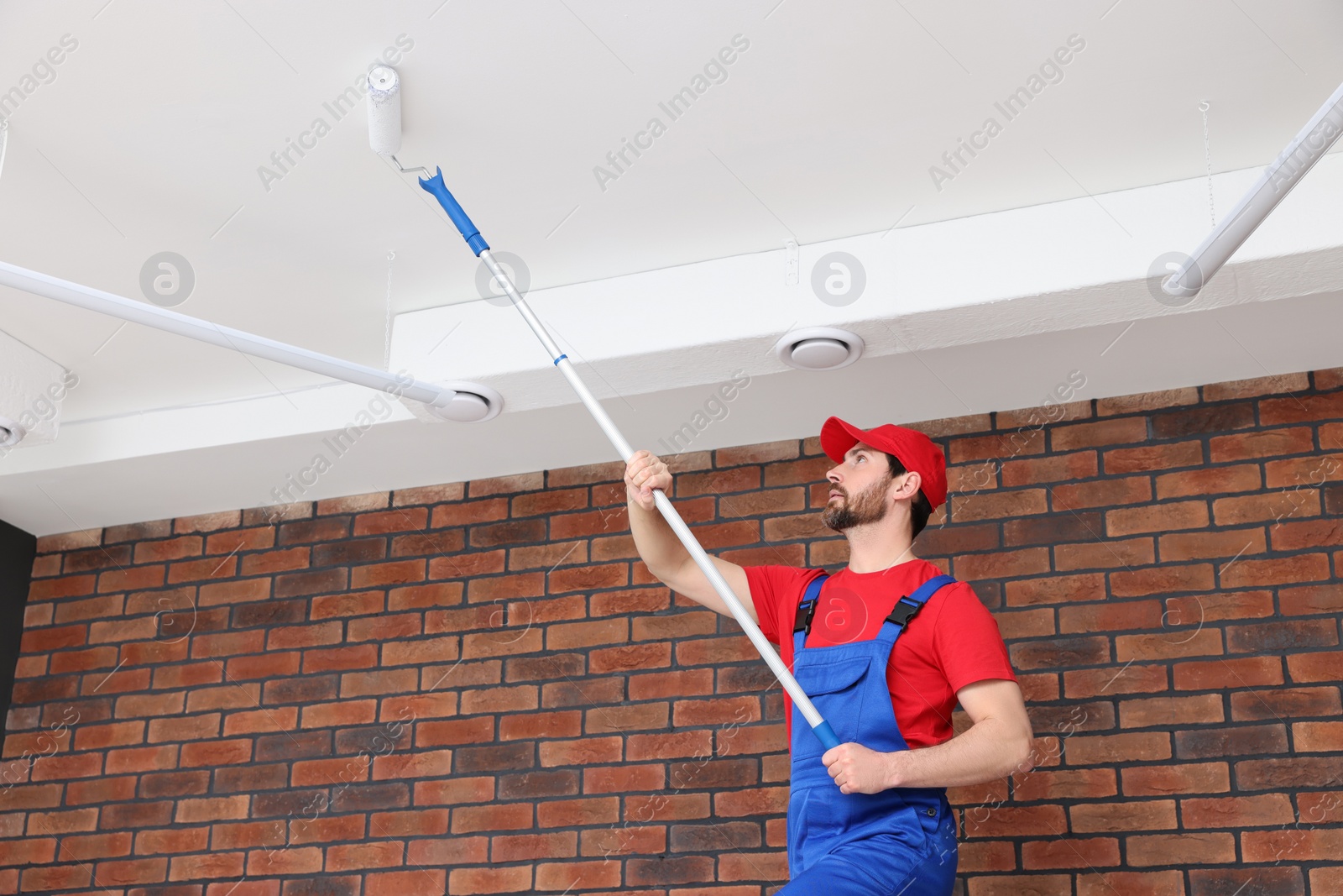 Photo of Handyman painting ceiling with roller in room