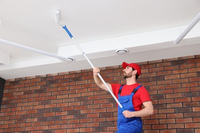 Handyman painting ceiling with roller in room