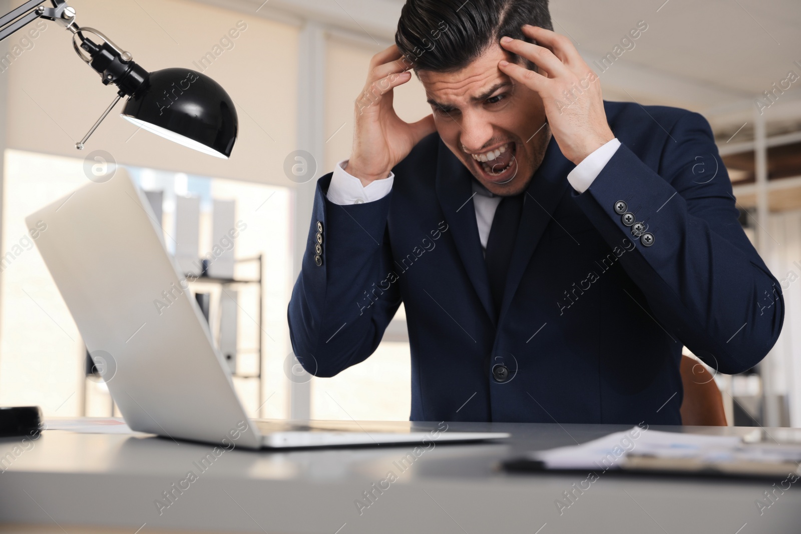 Photo of Emotional businessman with laptop at table in office