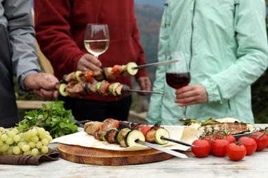 Photo of Friends having barbecue party outdoors, focus on table with delicious food