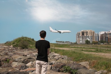Photo of Boy looking at airplane flying outdoors, back view
