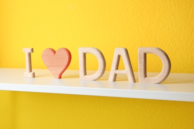 Photo of Phrase I LOVE DAD made of wooden letters on shelf near yellow wall