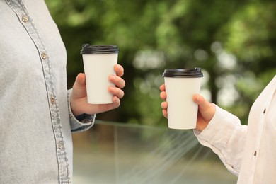 Photo of Women holding takeaway paper cups outdoors, closeup. Coffee to go
