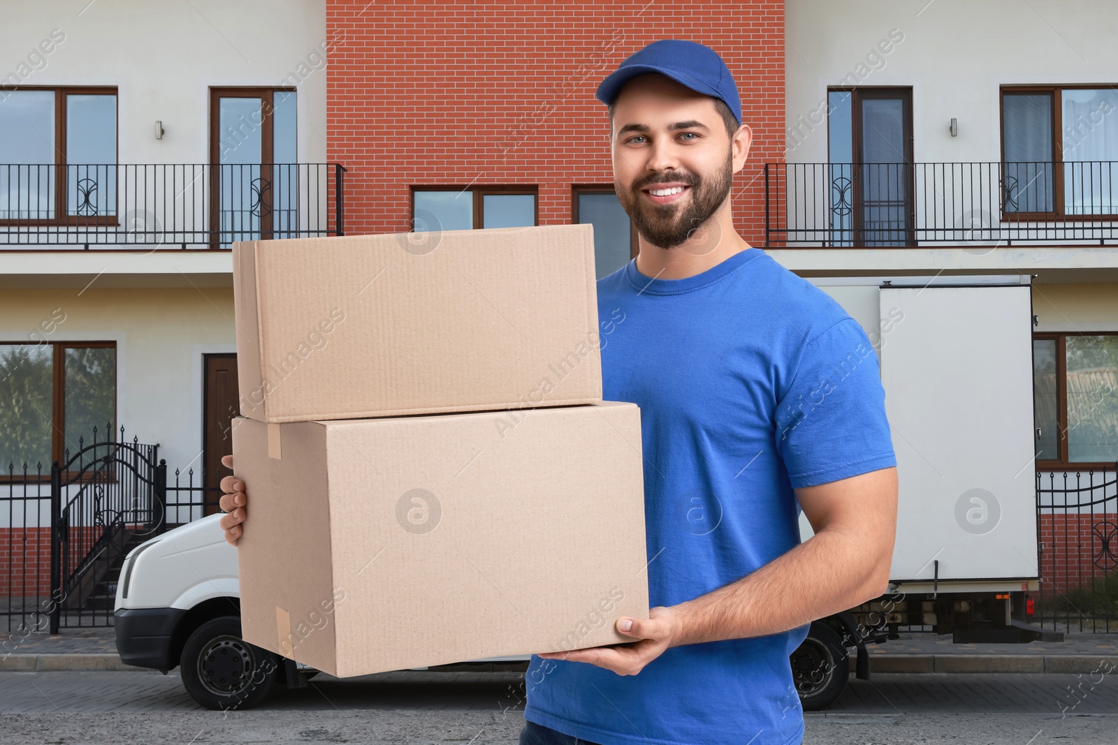 Image of Happy courier in uniform holding parcels outdoors