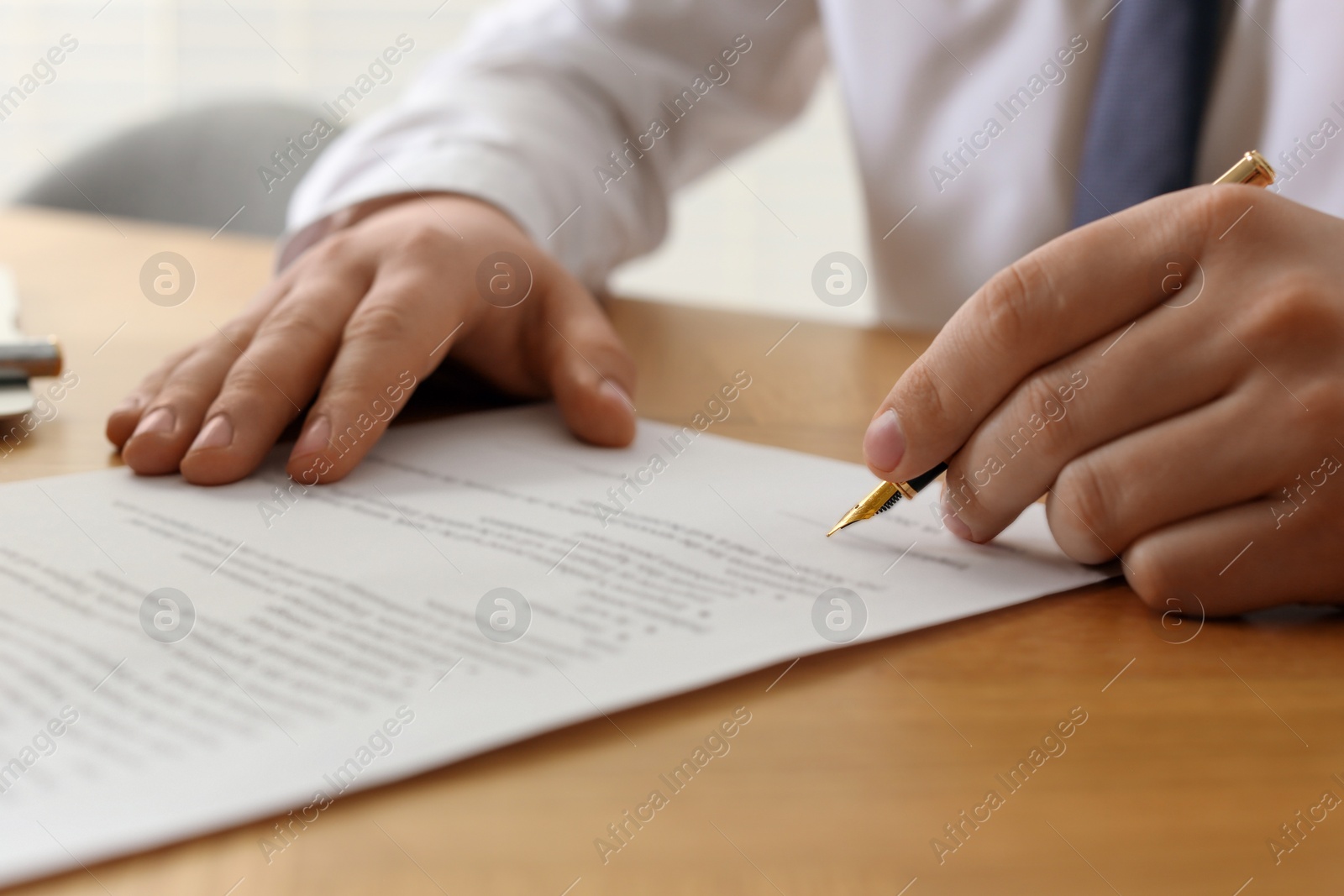 Photo of Notary signing document at wooden table indoors, closeup