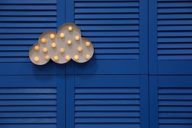 Photo of Stylish cloud shaped glowing night lamp hanging on blue folding screen. Space for text