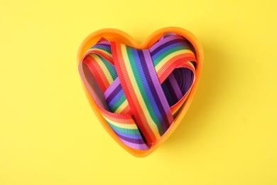 Heart shaped mold with bright rainbow ribbon on color background, top view. Symbol of gay community