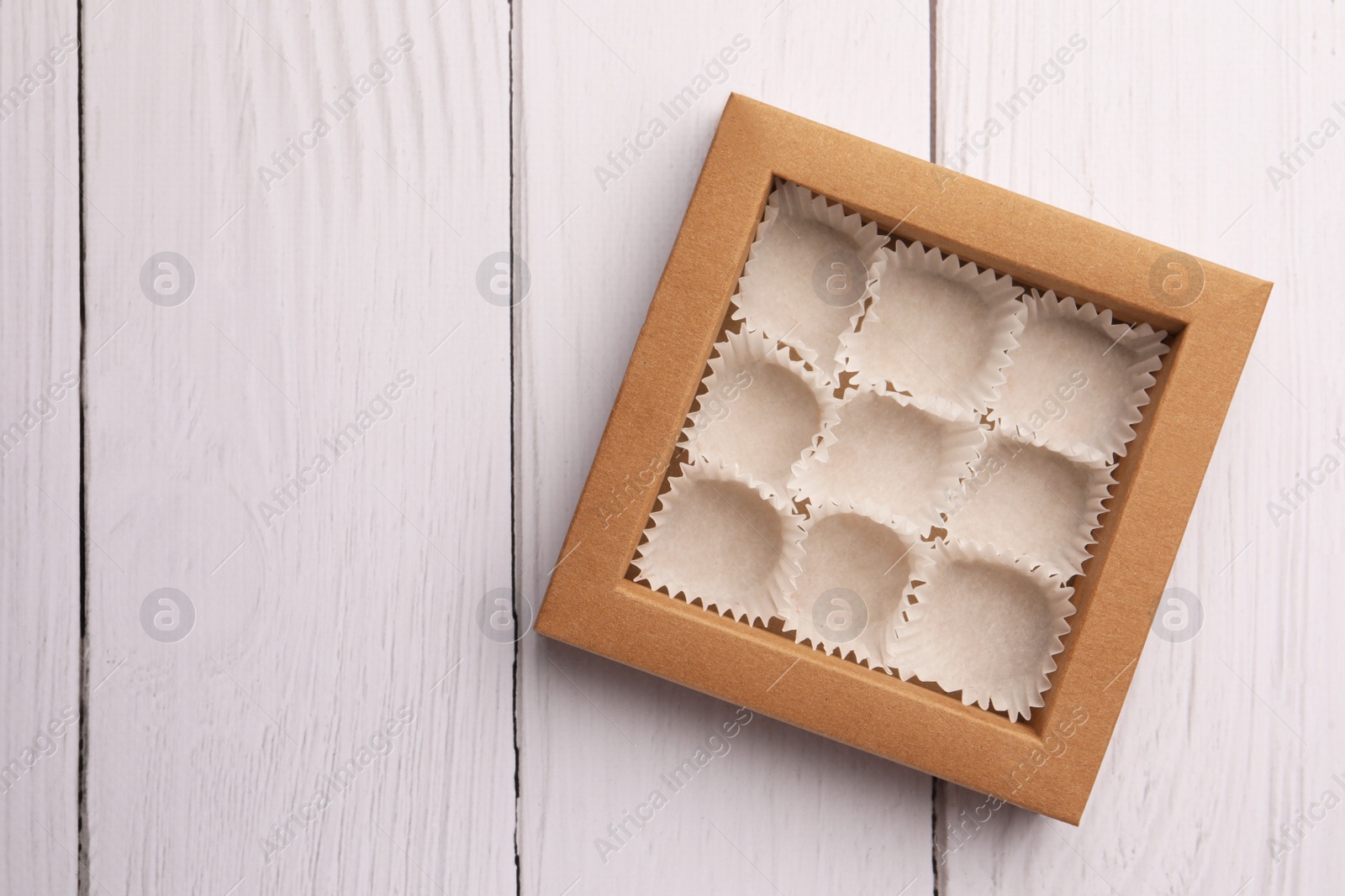 Photo of Empty box of chocolate sweets with candy paper cups on white wooden table, top view. Space for text