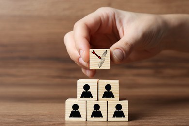 Image of Woman building pyramid of cubes with icons on wooden table, closeup. Target, arrow, magnifier and other illustrations