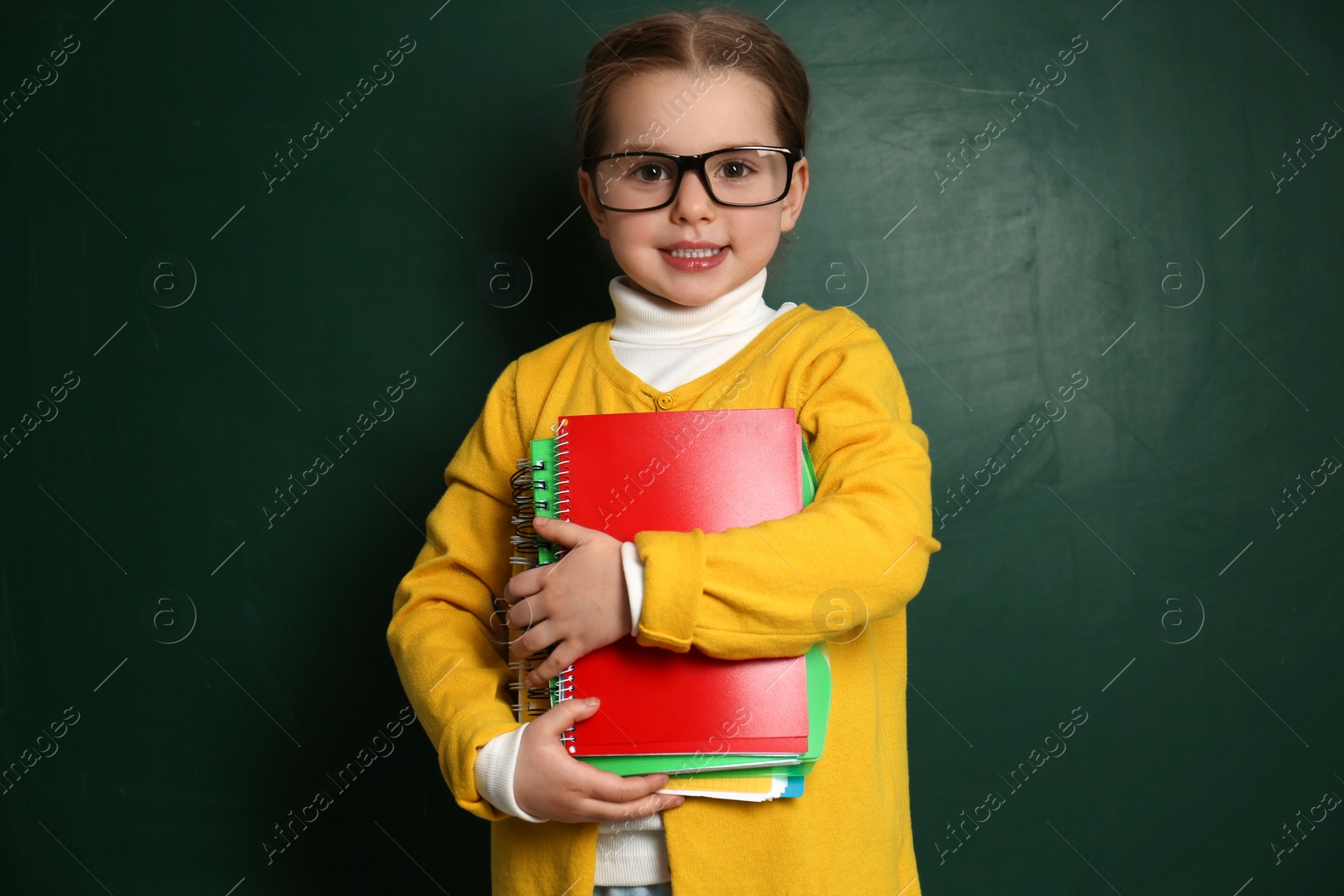 Photo of Cute little child wearing glasses near chalkboard. First time at school