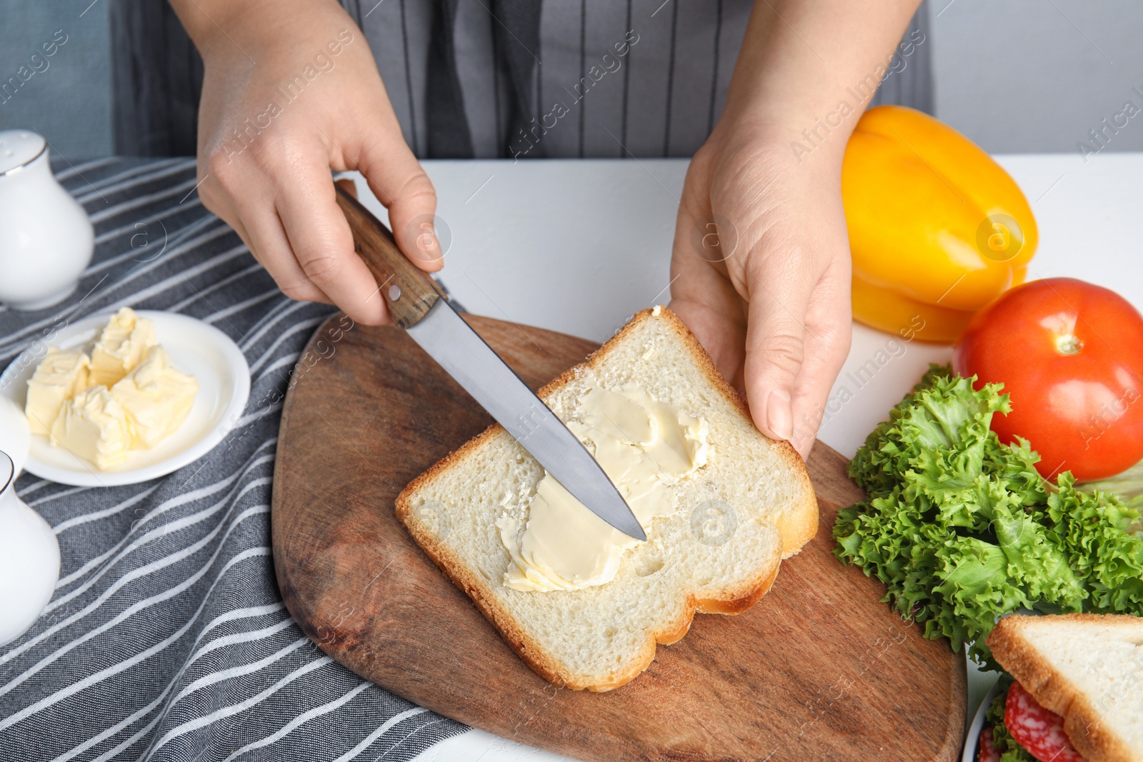 Photo of Woman spreading butter on sandwich at white table, closeup