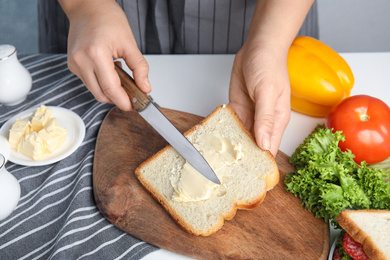 Photo of Woman spreading butter on sandwich at white table, closeup