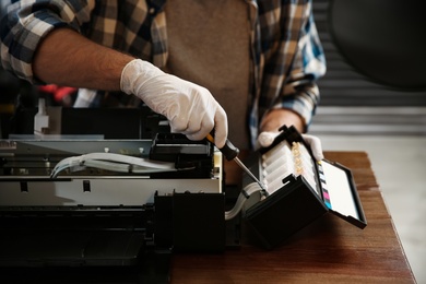 Repairman with screwdriver fixing modern printer indoors, closeup