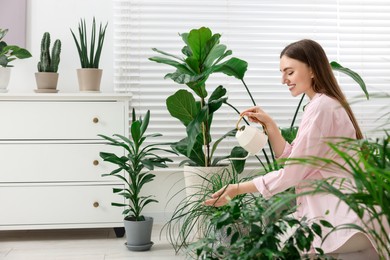 Photo of Beautiful young woman watering green houseplants at home