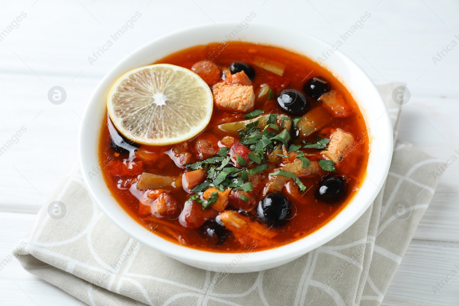 Photo of Meat solyanka soup with sausages, olives and vegetables on white wooden table, closeup