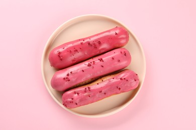 Photo of Delicious eclairs covered with glaze on pink background, top view