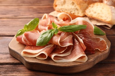 Photo of Slices of tasty cured ham and basil on wooden table, closeup