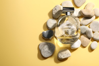 Bottle of luxury perfume in sunlight and stones on golden background, flat lay. Space for text