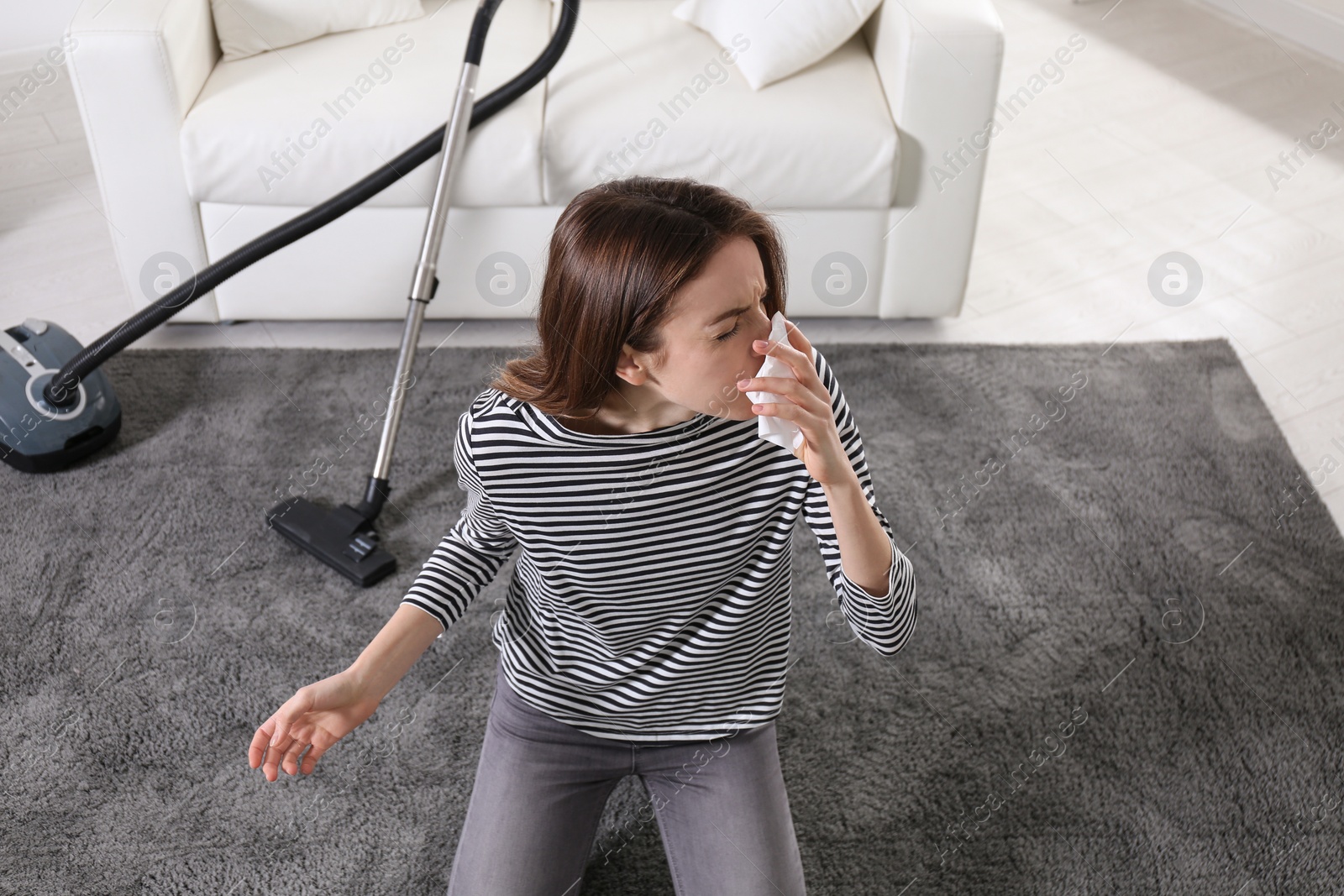 Photo of Young woman suffering from dust allergy while vacuuming house