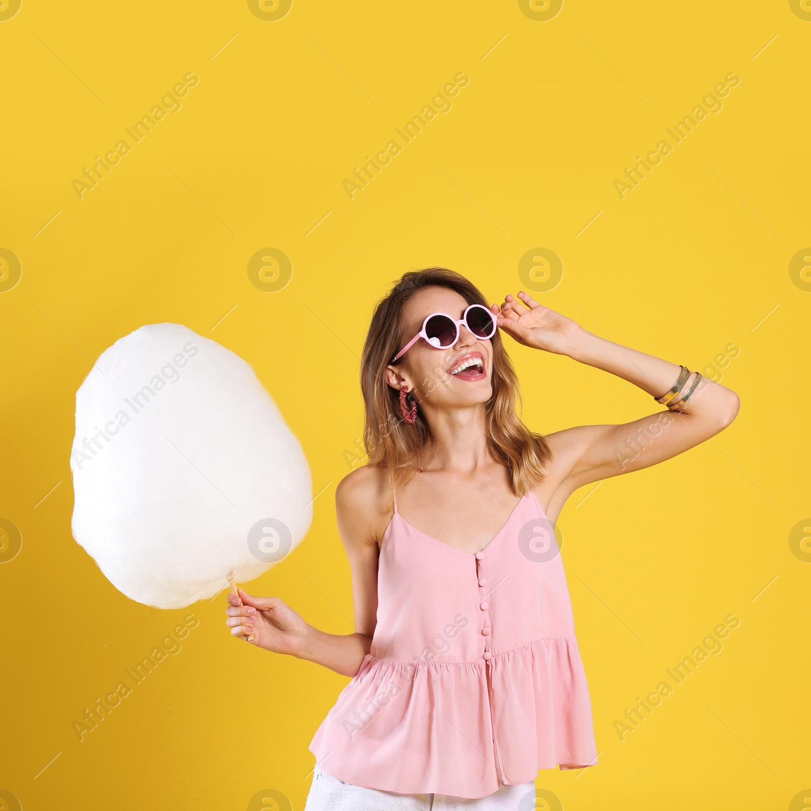 Photo of Happy young woman with cotton candy on yellow background