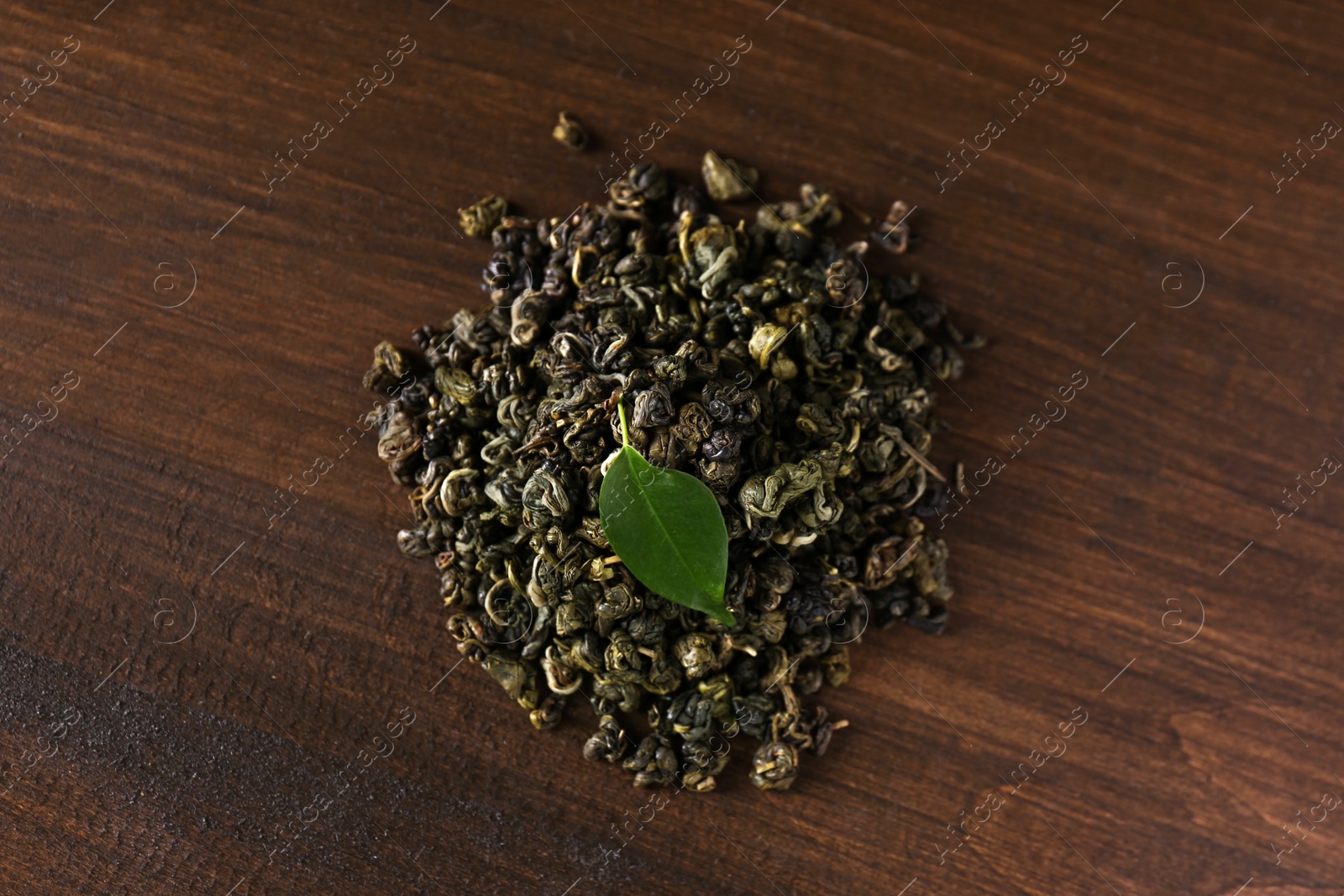 Photo of Heap of dried green tea leaves on wooden table, top view