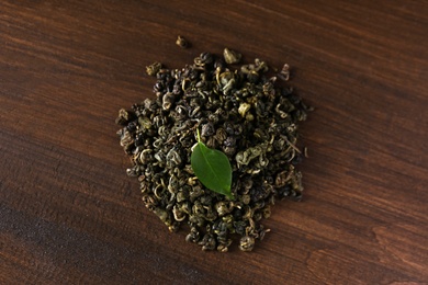 Photo of Heap of dried green tea leaves on wooden table, top view