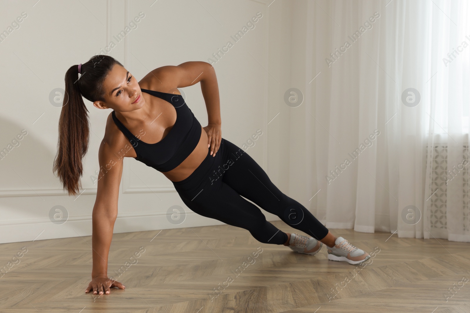 Photo of Young woman doing side plank exercise at home