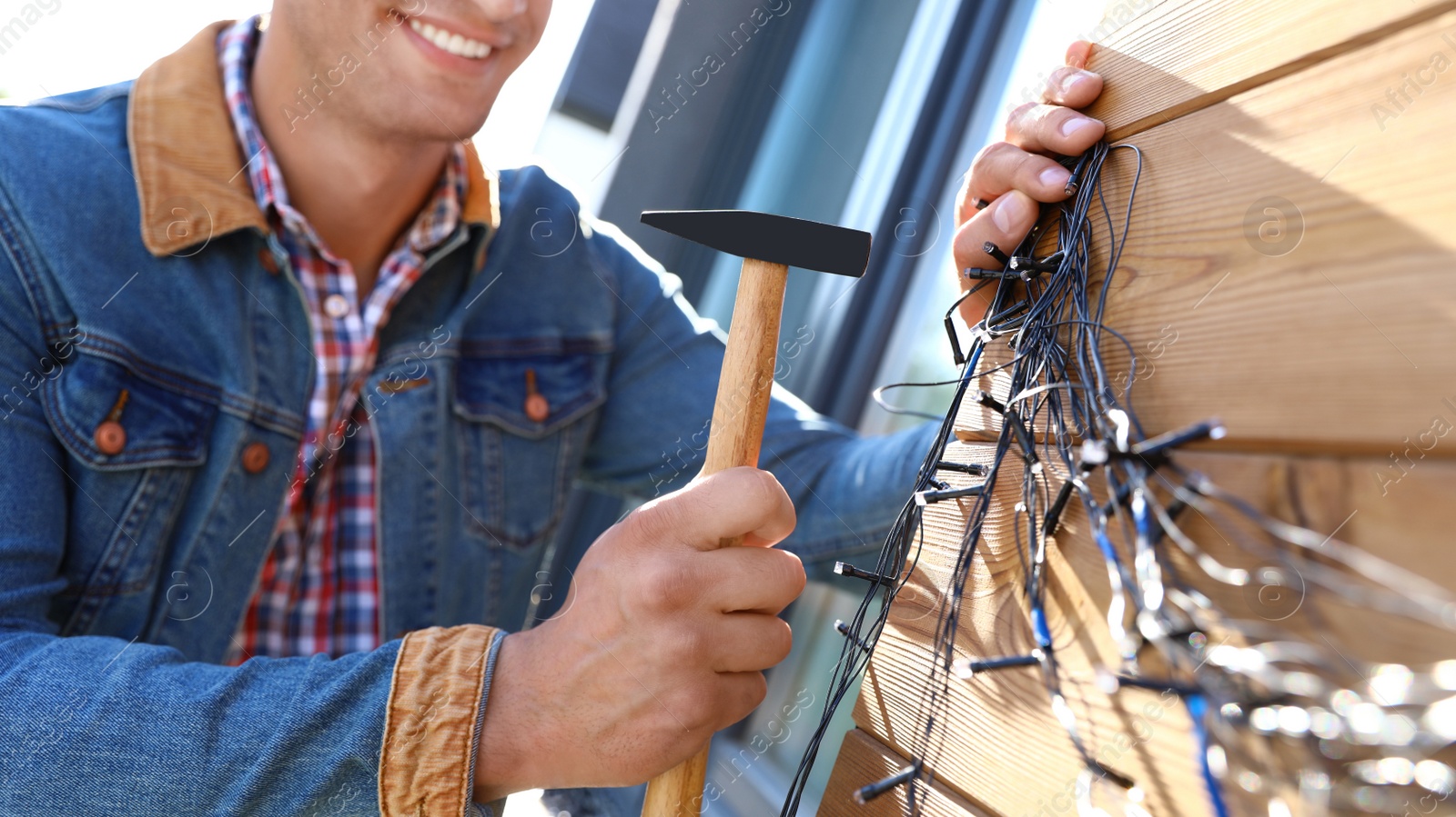 Photo of Man decorating house with Christmas lights outdoors, closeup