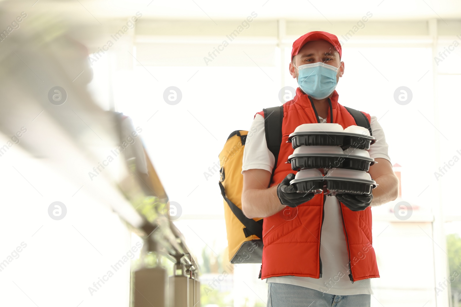 Photo of Courier in protective mask and gloves with order indoors. Restaurant delivery service during coronavirus quarantine