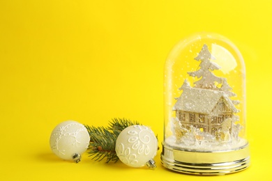 Photo of Beautiful snow globe, Christmas balls and fir branch on yellow background, space for text