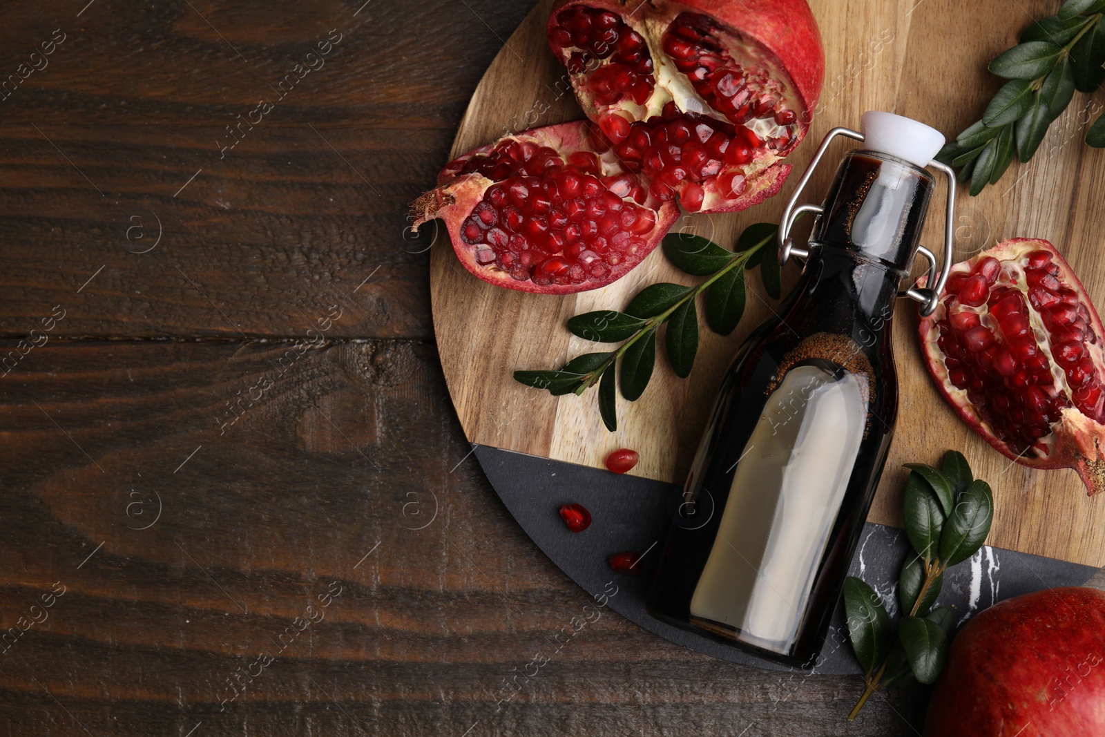 Photo of Tasty pomegranate sauce in bottle, fruits and branches on wooden table, top view. Space for text