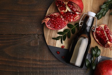 Photo of Tasty pomegranate sauce in bottle, fruits and branches on wooden table, top view. Space for text