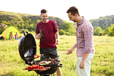 Young people having barbecue in wilderness. Camping season