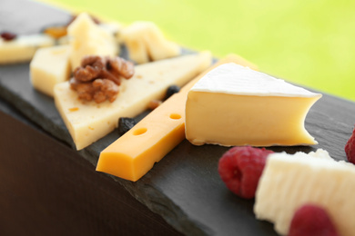 Photo of Different types of delicious cheeses and snacks on slate plate, closeup